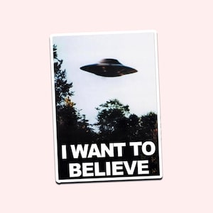 Può includere: Un adesivo raffigurante un UFO nero sopra una foresta, sullo sfondo di un cielo nuvoloso. Il testo "I WANT TO BELIEVE" è visualizzato in lettere bianche su un rettangolo nero.