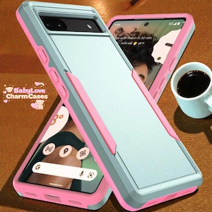 Puede incluir: Una funda protectora para teléfono con un diseño en capas. La funda presenta un centro azul claro, un marco gris y detalles en rosa. La funda se muestra con un teléfono que muestra una interfaz de aplicación y una taza de café.