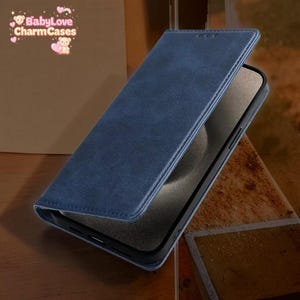 Puede incluir: Una funda de teléfono de cuero azul con tapa abatible. La funda está abierta, revelando la pantalla del teléfono. La funda tiene un borde cosido y un cierre magnético. La marca "BabyLove CharmCases" es visible en la esquina superior izquierda.