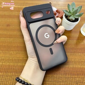 Puede incluir: Funda de teléfono negra con parte trasera transparente y diseño circular con la letra "G". La funda tiene un recorte para la cámara y un anillo magnético. Diseñada para un smartphone.