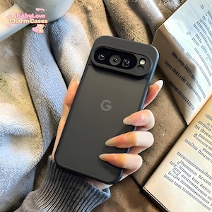 Puede incluir: Una funda de teléfono negra con un recorte para la cámara, con el logotipo de Google. La funda se sostiene en una mano con uñas largas. El texto "BabyLove CharmCases" es visible en la esquina superior izquierda.