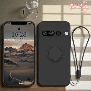 Puede incluir: Funda de teléfono negra con un recorte para la cámara, un agarre circular y una correa para la muñeca. La pantalla del teléfono muestra la hora 16:28 y la fecha 6 de noviembre, con un fondo de paisaje montañoso.