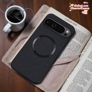 Puede incluir: Una funda de teléfono negra con un diseño circular y una lente de cámara se coloca sobre un libro abierto. Una taza de café blanca está a la izquierda. La funda tiene una apariencia texturizada. El libro está abierto en una página de texto.