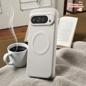 Puede incluir: Una funda de teléfono gris claro con un recorte para la cámara y un diseño circular en la parte posterior. Una taza blanca de café está al lado de la funda, con vapor saliendo de ella. El texto "BabyLove CharmCases" está en la esquina superior derecha.