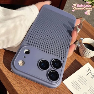 Puede incluir: Una funda de teléfono azul bígaro con una sección superior perforada y tres lentes de cámara. El texto "BabyLove Charm Cases" es visible. La funda se sostiene sobre una superficie de madera.