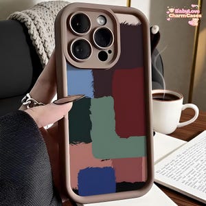 May include: A phone case with a colorful abstract design. The case features a tan border and a back panel with brushstroke-style blocks of blue, green, red, and brown. The case has a camera cutout and the text "BabyLove CharmCases".