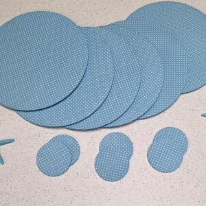 May include: A collection of blue placemats and coasters with a white polka dot pattern. The placemats are round, and the coasters are oval-shaped. Two blue starfish decorations are also included.