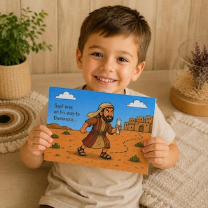 May include: A young child smiles while holding a children's book. The book features an illustration of a man in a brown robe walking on a desert path, with the text "Saul was on his way to Damascus..." against a blue sky.