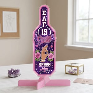 May include: A vertical bottle-shaped acrylic display stand in shades of purple and pink. The design features Greek letters, the number 19, the text Chapter Name, a hand gesture, pink roses, crystals, and the text SPR26 Name on a starry background.