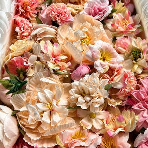Puede incluir: Una colecci&oacute;n de flores artificiales en tonos melocot&oacute;n, rosa suave y crema. El arreglo presenta varios tipos de flores, incluyendo peon&iacute;as, dalias y flores m&aacute;s peque&ntilde;as con p&eacute;talos en capas, tallos verdes y centros amarillos.