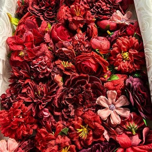 Puede incluir: Una colecci&oacute;n de flores artificiales en varios tonos de rojo intenso, burdeos y granate, empaquetadas estrechamente. El surtido incluye m&uacute;ltiples tipos de flores con p&eacute;talos en capas, algunas con centros amarillos y otras con detalles rosados.