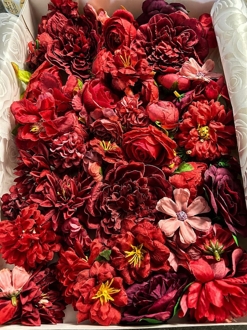 Puede incluir: Una colecci&oacute;n de flores artificiales en varios tonos de rojo intenso, burdeos y granate, empaquetadas estrechamente. El surtido incluye m&uacute;ltiples tipos de flores con p&eacute;talos en capas, algunas con centros amarillos y otras con detalles rosados.