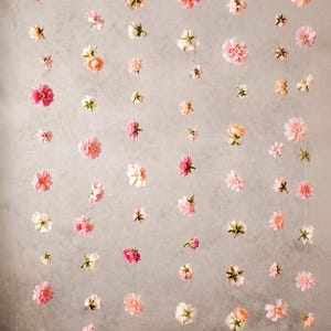 Puede incluir: Un colgante decorativo de pared con 60 flores dispuestas en hilos verticales. Las flores artificiales presentan diversos tonos de rosa, melocot&oacute;n y blanco, suspendidas mediante hilos finos y transparentes. El texto 60 FLOWERS aparece arriba.