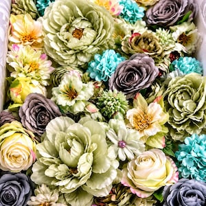Puede incluir: Una colecci&oacute;n de flores artificiales en varios tonos de verde salvia, morado polvoriento, crema y turquesa brillante. El arreglo presenta p&eacute;talos en capas de rosas, peon&iacute;as y peque&ntilde;as flores de relleno, creando una exhibici&oacute;n floral densa.