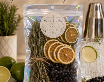 Puede incluir: Una bolsa transparente e iridiscente que contiene un kit de guarnición para gin tonic con ramas de romero seco atadas con cuerda, rodajas de cítricos deshidratados y bayas de enebro. La etiqueta circular dice Willow Stem Crafts Sip Kits.
