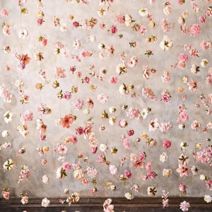 May include: A decorative backdrop featuring numerous individual pink, white, and peach-colored flowers suspended on thin, vertical strings. The floral arrangement creates a floating effect against a neutral, mottled gray wall surface.