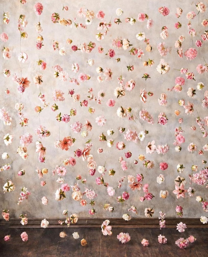 Puede incluir: Un tel&oacute;n de fondo decorativo con numerosas flores individuales de color rosa, blanco y melocot&oacute;n suspendidas en hilos verticales finos. El arreglo floral crea un efecto flotante contra una pared gris neutra y moteada.