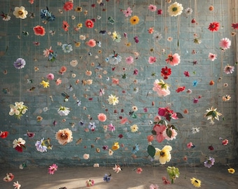 Puede incluir: Una gran colección de diversas flores artificiales en tonos rojos, rosas, amarillos, blancos y azules, suspendidas individualmente de hilos finos a diferentes alturas, creando un efecto flotante contra una pared de ladrillo azul claro.