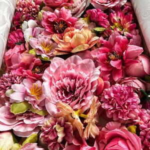 Puede incluir: Una colecci&oacute;n de flores artificiales en varios tonos de rosa, magenta y melocot&oacute;n. El arreglo presenta m&uacute;ltiples tipos de flores, incluyendo rosas, peon&iacute;as y flores m&aacute;s peque&ntilde;as con centros amarillos, todas agrupadas estrechamente.