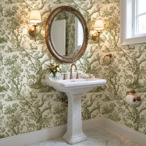 May include: A white marble pedestal sink with a brass faucet, positioned beneath an oval mirror with a dark wood frame. Two brass wall sconces with white shades flank the mirror, set against wallpaper featuring a green and white forest motif.