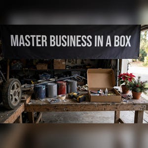 May include: A black banner with the white text MASTER BUSINESS IN A BOX hangs above a wooden workbench. The table holds several paint cans, a pressure washer wand, a yellow and black power drill, and an open cardboard box containing supplies.