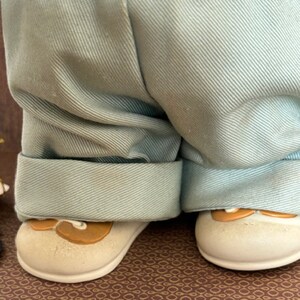 Puede incluir: Un par de pantalones azul claro con los pu&ntilde;os enrollados. Los pantalones son usados por una mu&ntilde;eca con zapatos marrones.