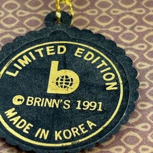 Puede incluir: Etiqueta negra y dorada con el texto "Limited Edition" y "Brinn's 1991 Made in Korea" alrededor de un logotipo de una "b" con un globo terr&aacute;queo dentro.