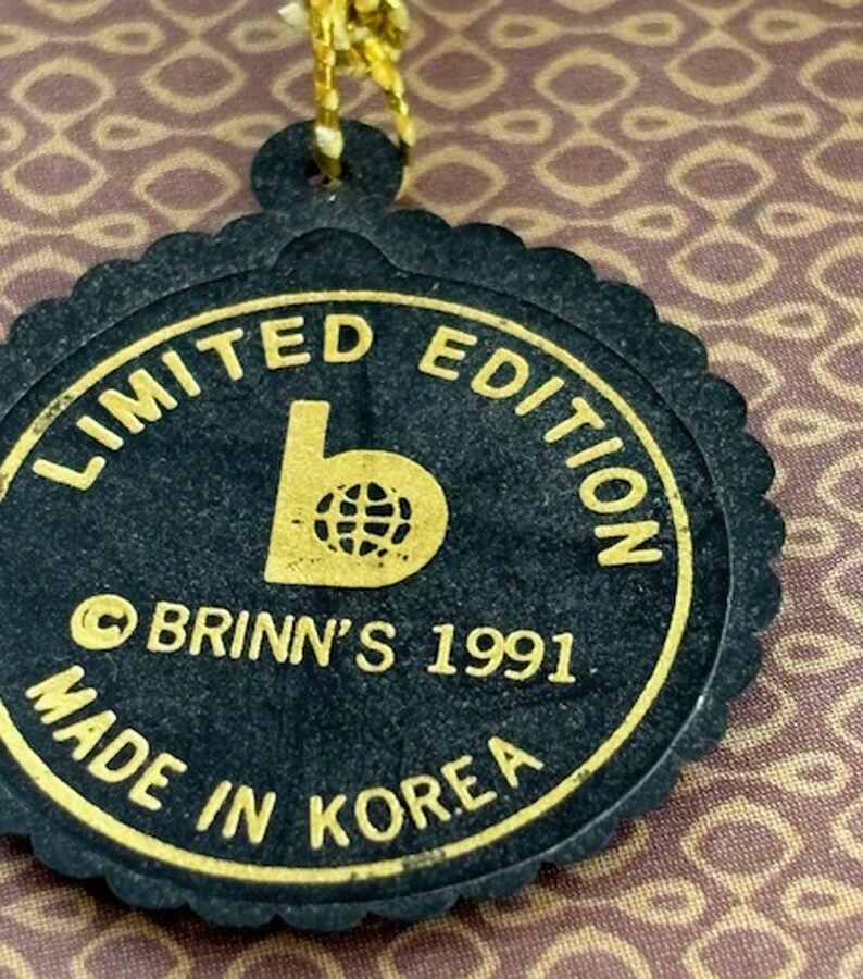 Puede incluir: Etiqueta negra y dorada con el texto "Limited Edition" y "Brinn's 1991 Made in Korea" alrededor de un logotipo de una "b" con un globo terr&aacute;queo dentro.