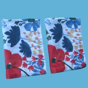 May include: Two white fabric tea towels with a floral pattern. The pattern features red, blue, and yellow flowers on a white background.