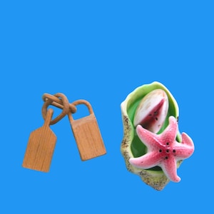 May include: A set of salt and pepper shakers shaped like a seashell and a starfish. The seashell is green and white with a pink watermelon slice inside. The starfish is pink with a white center and black dots.
