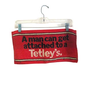 Paño de cocina promocional vintage de Tetley, rojo y negro, con el logo &quot;Un hombre puede encariñarse con un Tetley&#39;s&quot;.