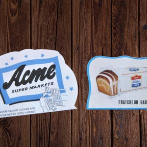May include: Two vintage advertising signs. The first sign is blue and white with the text "Acme Super Markets" and the slogan "Where quality counts and your money goes furthest". The second sign is blue and white with a loaf of bread and the text "Fraicheur Garantie".