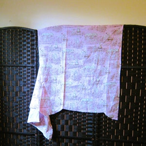 May include: A pink fabric with a white and blue floral pattern. The fabric is draped over a black wicker screen.
