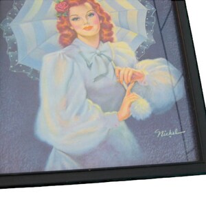 Op de afbeelding: Een ingelijste vintage illustratie van een vrouw met rood haar die een witte jurk draagt en een wit-blauwe gestreepte parasol vasthoudt. De vrouw glimlacht en kijkt naar de kijker. De illustratie is rechtsonder getekend met "Nickel".