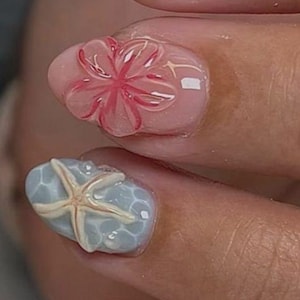 May include: Close-up of manicured nails with a beach theme. Designs include a seashell, a pink flower, a starfish on a blue background, and a nail with red dots. The nails are painted with a clear, glossy finish.