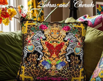 May include: Square decorative pillow with a leopard print background and a central design featuring two zebras, cherubs, and ornate gold detailing. The pillow has a black border and the text "Zebras and Cherubs".