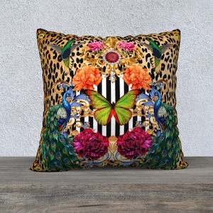 May include: Square decorative pillow with a leopard print background. The pillow features a central design with a butterfly, flowers, peacocks, and ornate gold accents. The color palette includes gold, black, white, red, green, and blue.