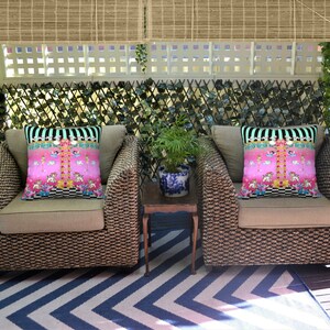 May include: Two wicker chairs with beige cushions and pink and black patterned throw pillows. The chairs are on a black and white chevron patterned rug.