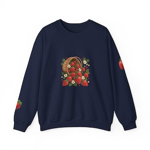 May include: A navy blue crewneck sweatshirt featuring a central graphic of a woven basket spilling over with bright red strawberries, green leaves, and small white flowers. Additional single strawberry illustrations appear on each long sleeve.