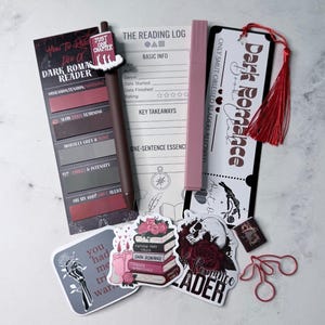 May include: A selection of dark romance themed stationery. Includes a reading log, bookmarks, stickers, a pen with a decorative top, and a pink highlighter. The items feature text such as "Dark Romance" and "How to Read Like a Dark Romance Reader."