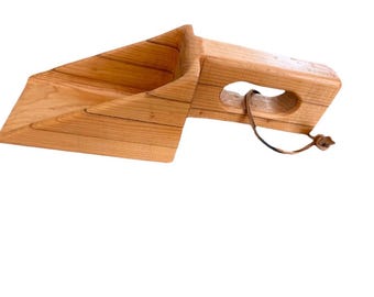 Op de afbeelding: Een lichtbruine houten schep met een brede, schuine kom en een dik handvat met een uitsparing voor de grip. Een dun, donkerbruin leren koord is door de opening in het handvat gestoken, zodat het keukengereedschap gemakkelijk kan worden opgehangen.