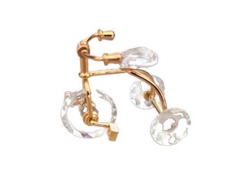 Op de afbeelding: Een goudkleurige metalen broche in de vorm van een fiets, voorzien van heldere, gefacetteerde kristallen accenten die de wielen en het zadel vormen. Het ontwerp bevat een gebogen frame, een stuur en een kleine speldsluiting voor bevestiging.