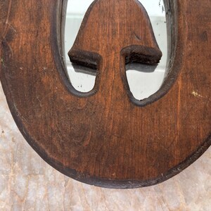 May include: A circular wooden mirror frame with a dark brown finish and a visible wood grain texture. The frame features a central cutout in the shape of a mushroom, with the reflective mirror surface visible through the opening of the cutout.