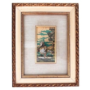 May include: A rectangular framed artwork featuring a central vertical print of a landscape with a large rock formation, trees, and a teal sky. The print is set within a textured off-white mat and a decorative gold and brown ornate wooden frame.