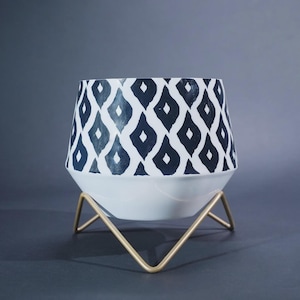 May include: A tapered planter featuring a white base and a navy blue diamond pattern on the upper section. The planter is supported by a gold-toned metal wire stand with four angled legs that provide a stable base for the container.