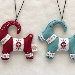 May include: Two felt Christmas ornaments shaped like goats. One is red with white accents and the other is blue with white accents. Both have a white star on their back.