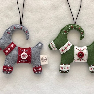 May include: Two felt Christmas ornaments shaped like goats. One goat is gray with red and white accents, the other is green with red and white accents.