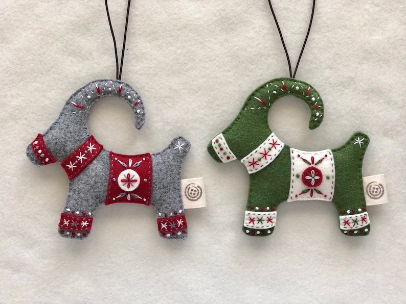 May include: Two felt Christmas ornaments shaped like goats. One goat is gray with red and white accents, the other is green with red and white accents.