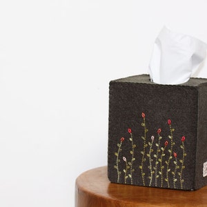 May include: A dark gray felt tissue box cover with an embroidered design of green stems and red flowers.