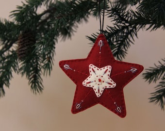 May include: A red felt star ornament with white felt accents and a beaded center. The star is hanging from a tree branch.